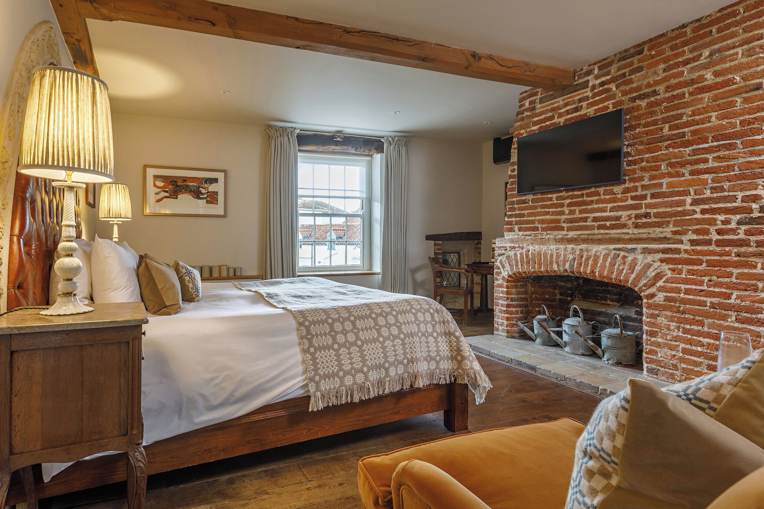 Un dormitorio con una cama grande, una mesita de noche de madera, una lámpara, una chimenea y una ventana con cortinas.