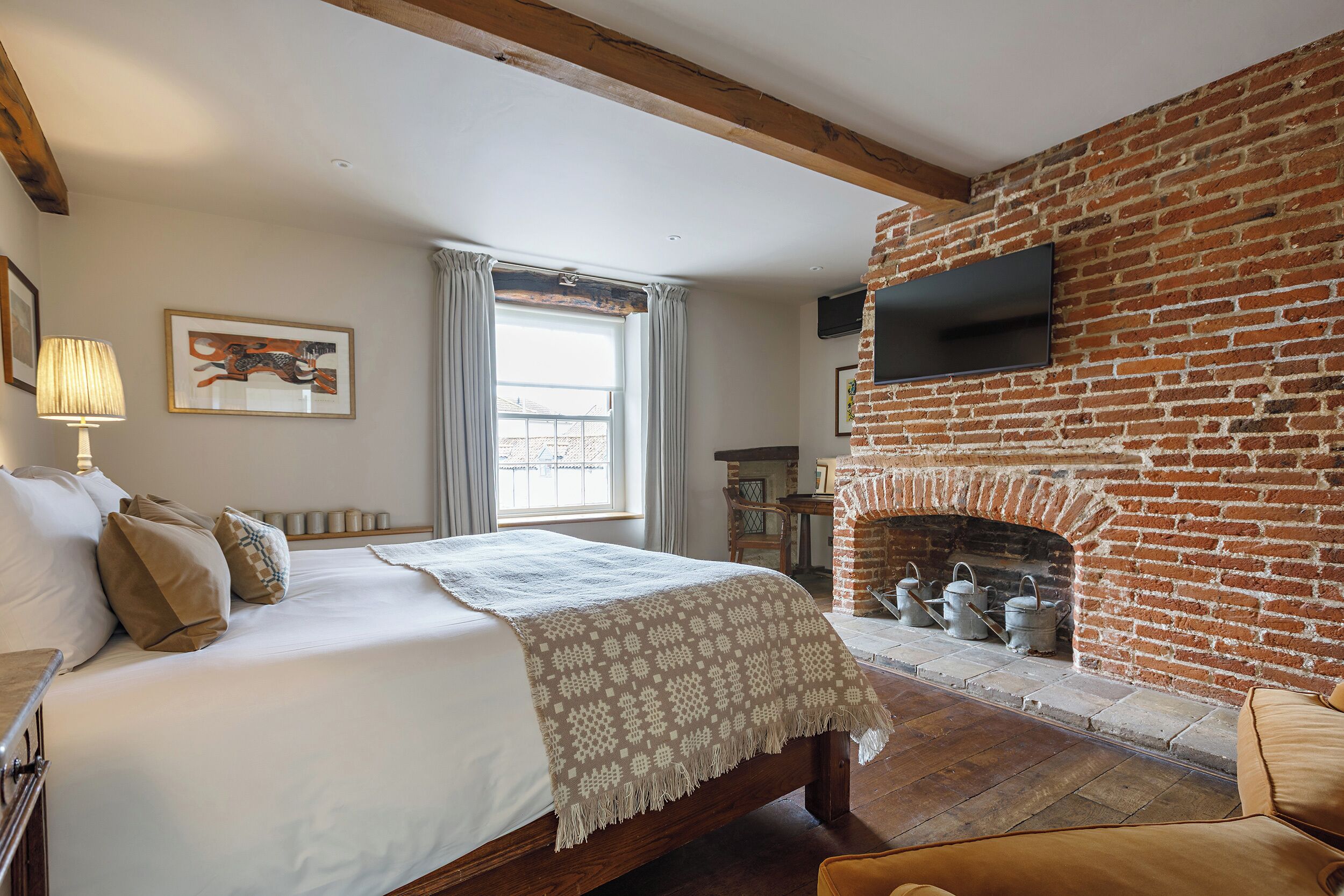 A bedroom with a large bed, a brick fireplace, and a television mounted on the wall.