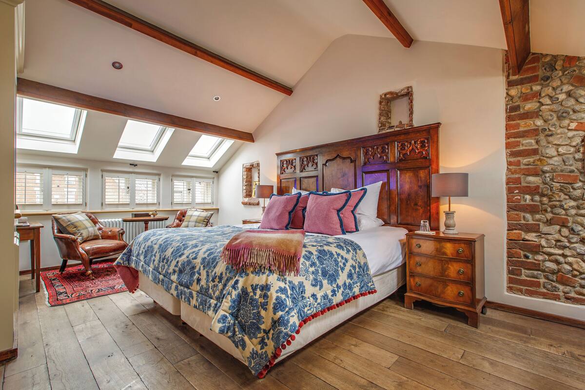 A bedroom with a large bed, wooden headboard, a stone wall, and skylights.