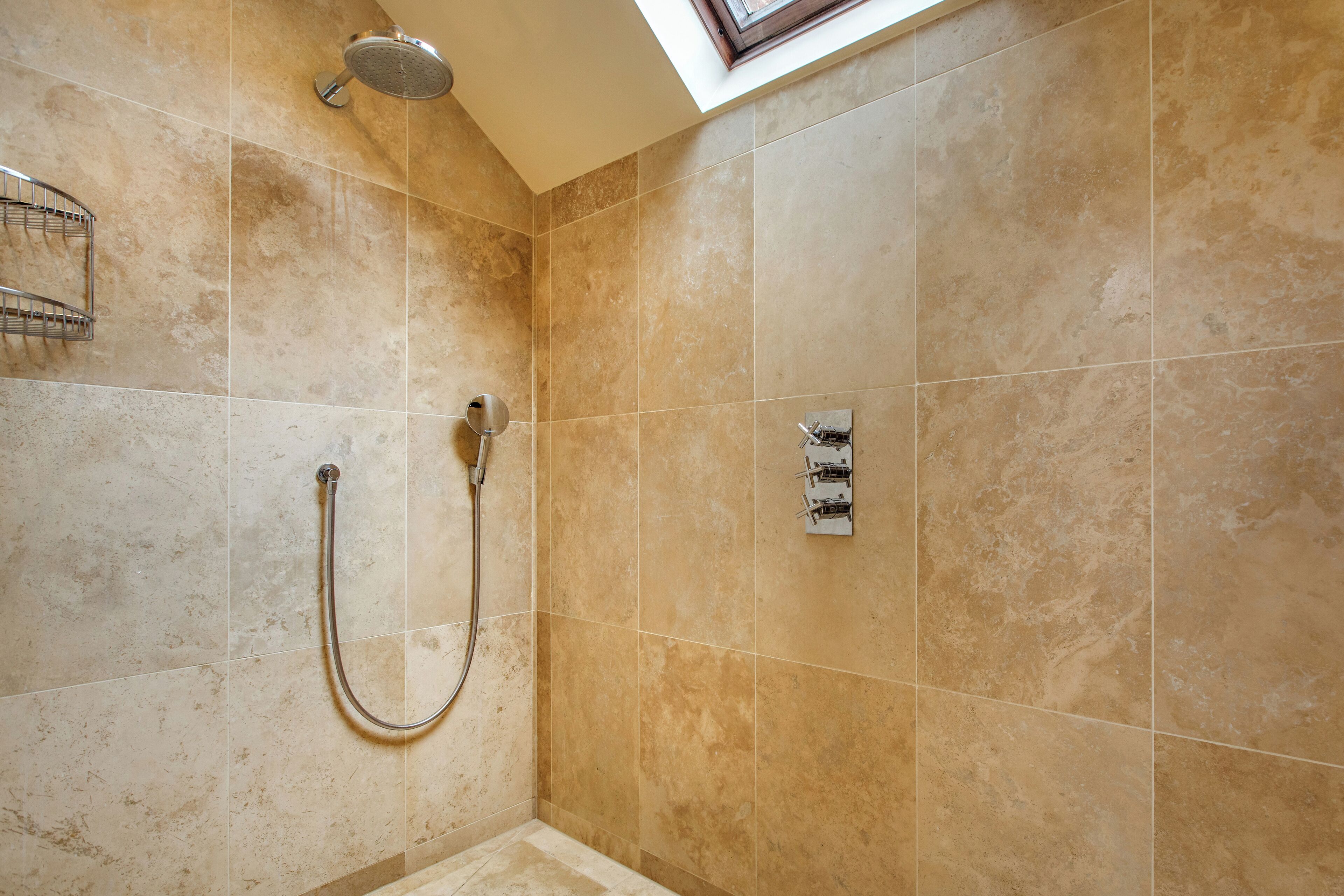 A shower area with beige tiles, a handheld showerhead, and a wall-mounted control panel.
