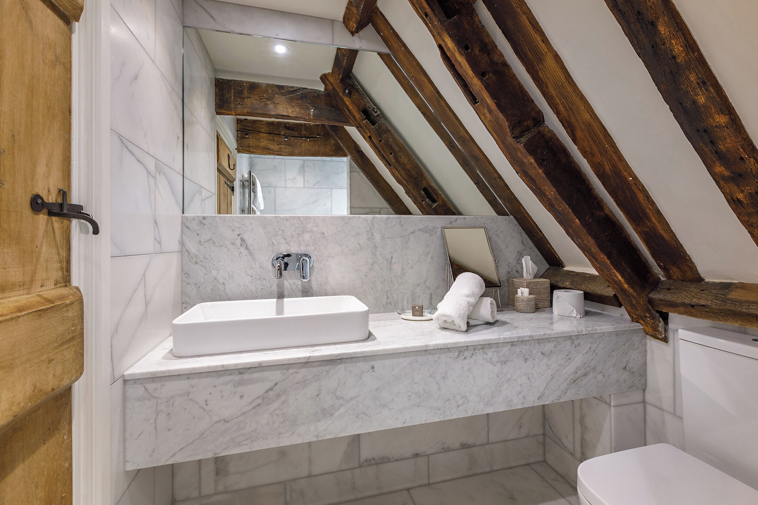 A bathroom with a marble sink, wooden beams, and a toilet.