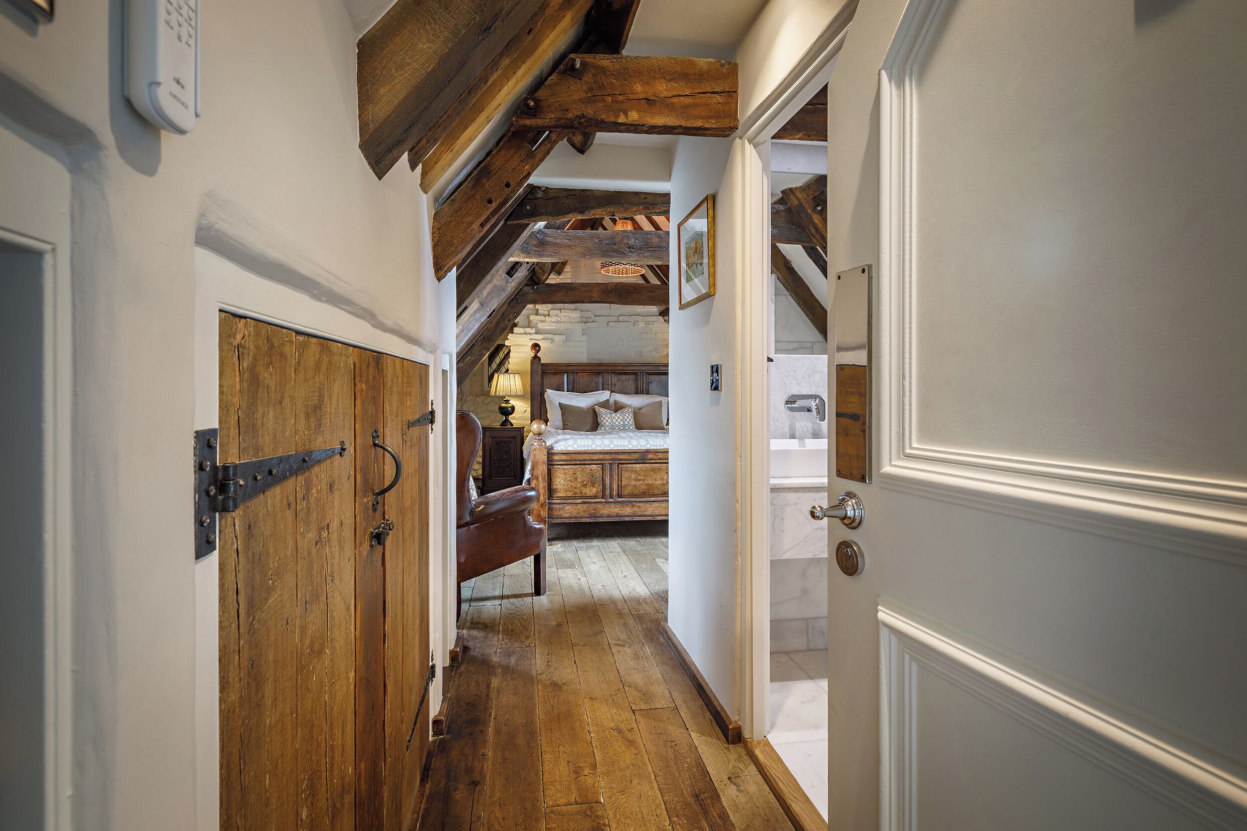 Un couloir étroit doté d’un plancher en bois, d’une porte rustique et de poutres apparentes.