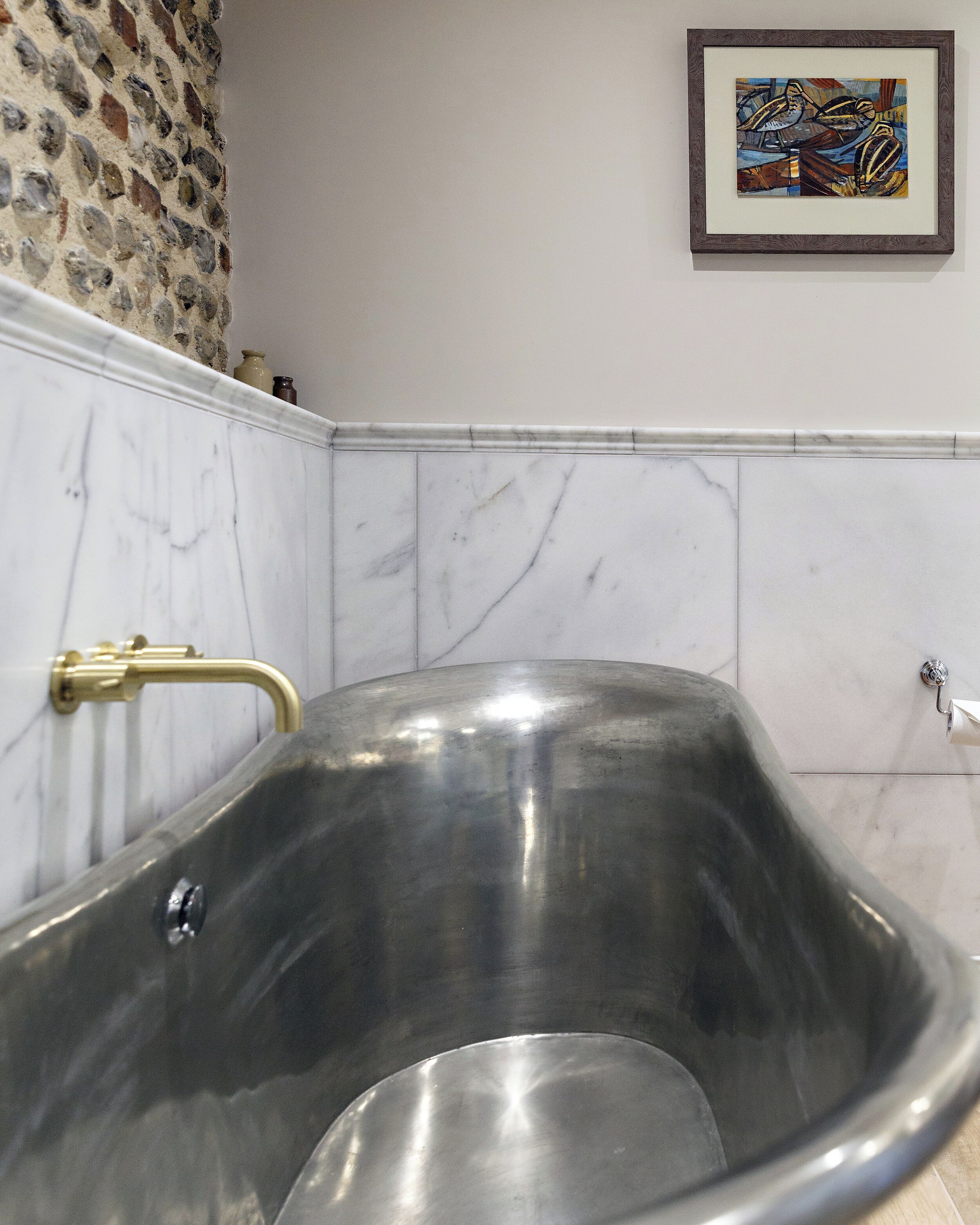 A modern bathroom with a freestanding bathtub, marble walls, and a framed artwork above the tub.