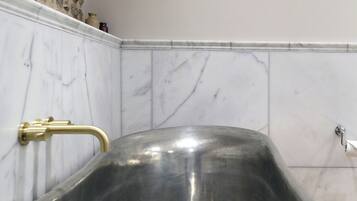 A modern bathroom with a freestanding bathtub, marble walls, and a framed artwork above the tub.