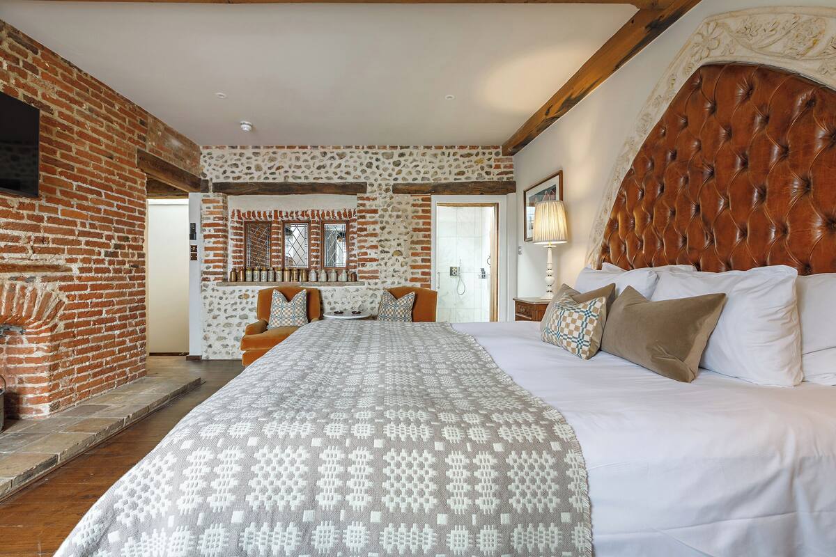 A bedroom with a large bed, a stone wall, and a wooden ceiling.