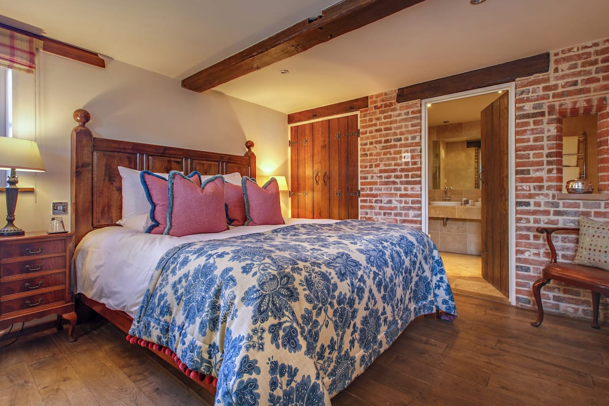 A bedroom with a wooden bed, a nightstand, a dresser, and a brick wall.
