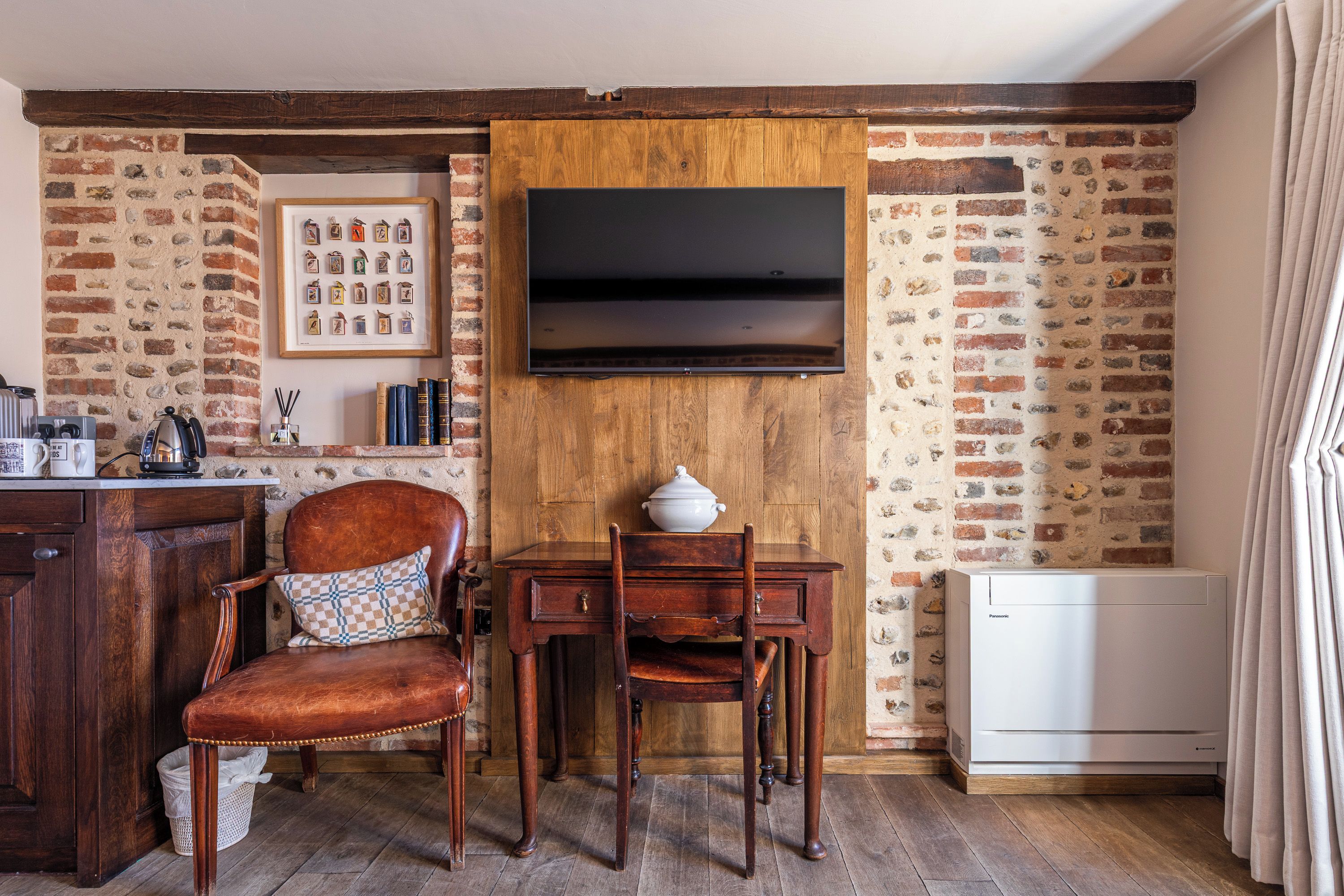 Una habitación rústica con pared de ladrillo, muebles de madera, un televisor de pantalla plana montado y un radiador blanco.