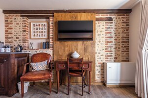 Una habitación rústica con pared de ladrillo, muebles de madera, un televisor de pantalla plana montado y un radiador blanco.