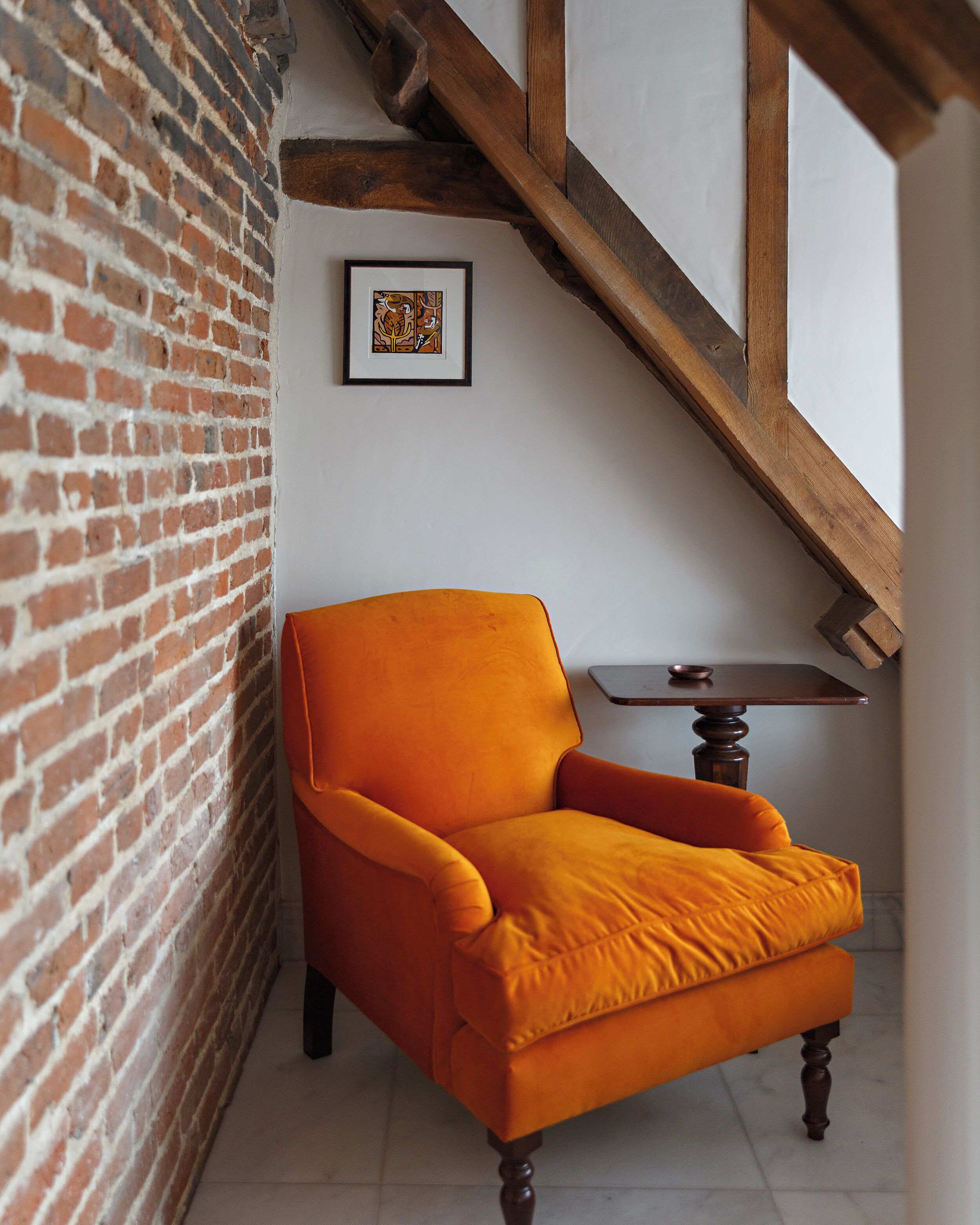 Ein Zimmer mit Backsteinwand, einer Holztreppe, einem gerahmten Kunstwerk und einem Holztisch mit Stuhl.