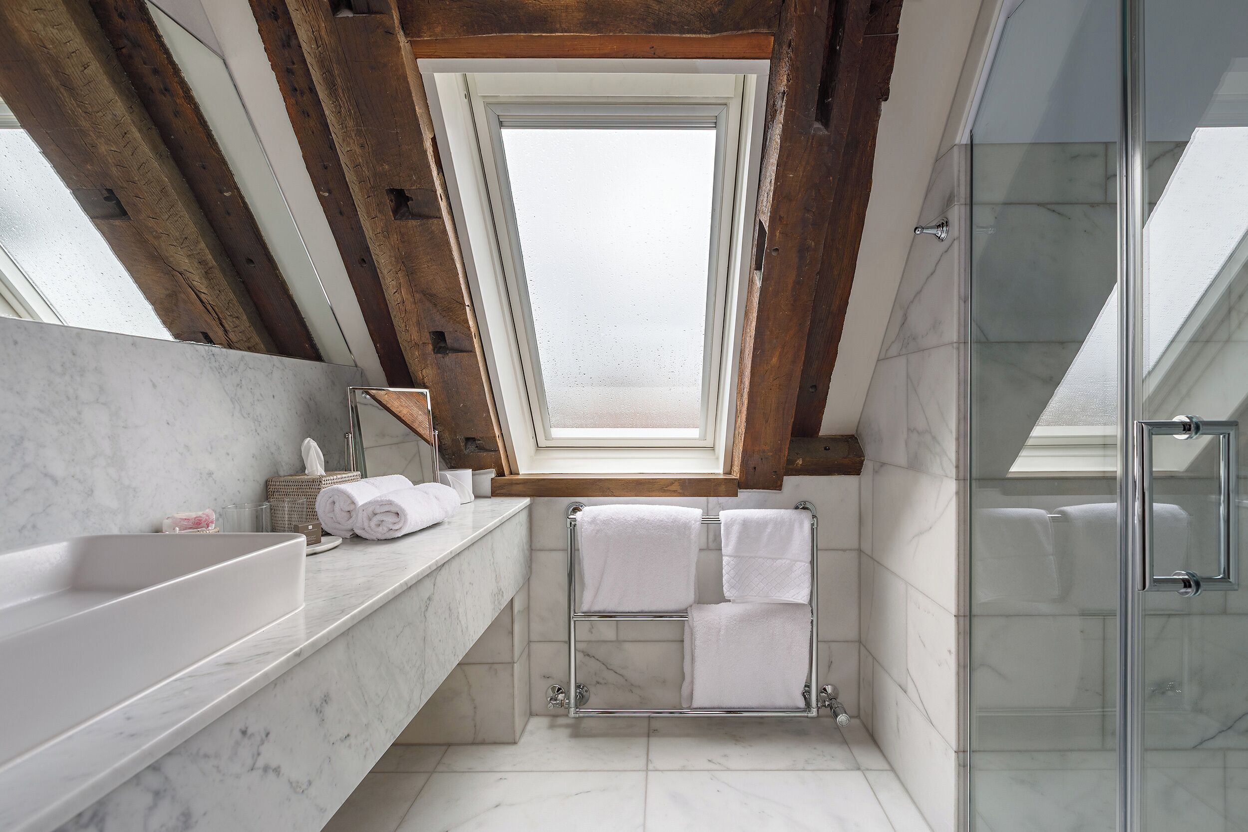 A modern bathroom with a skylight, a glass shower, and a marble countertop.