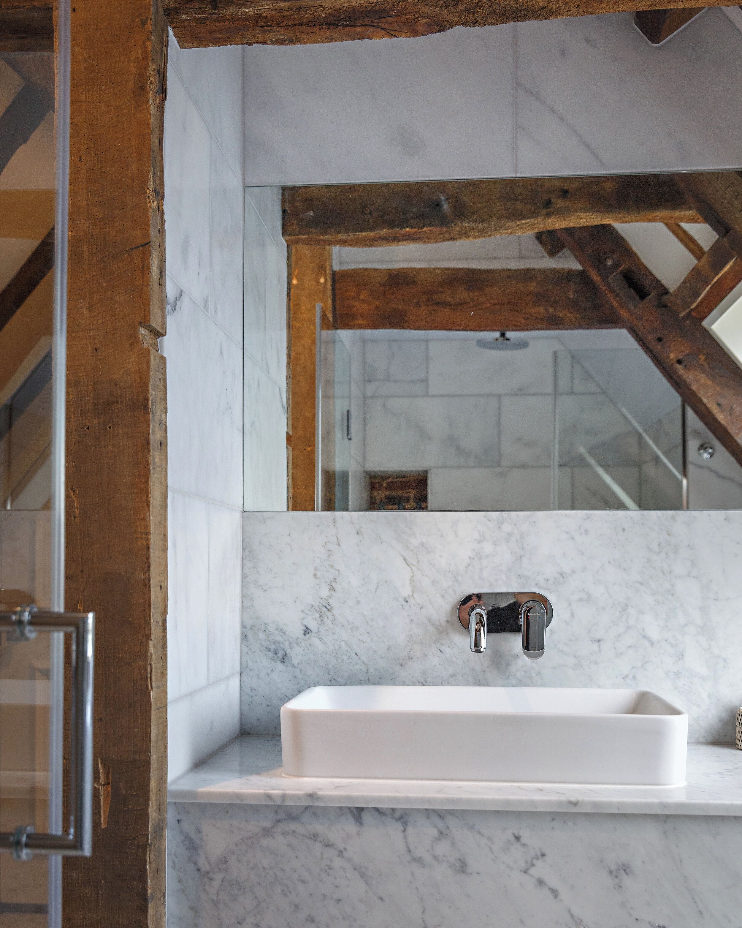 A bathroom with a white sink, marble walls, and wooden beams.