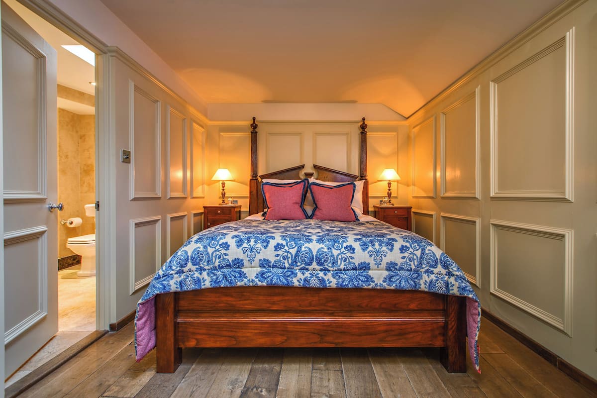 A bedroom with a wooden bed, two bedside tables, and a bathroom visible through an open door.