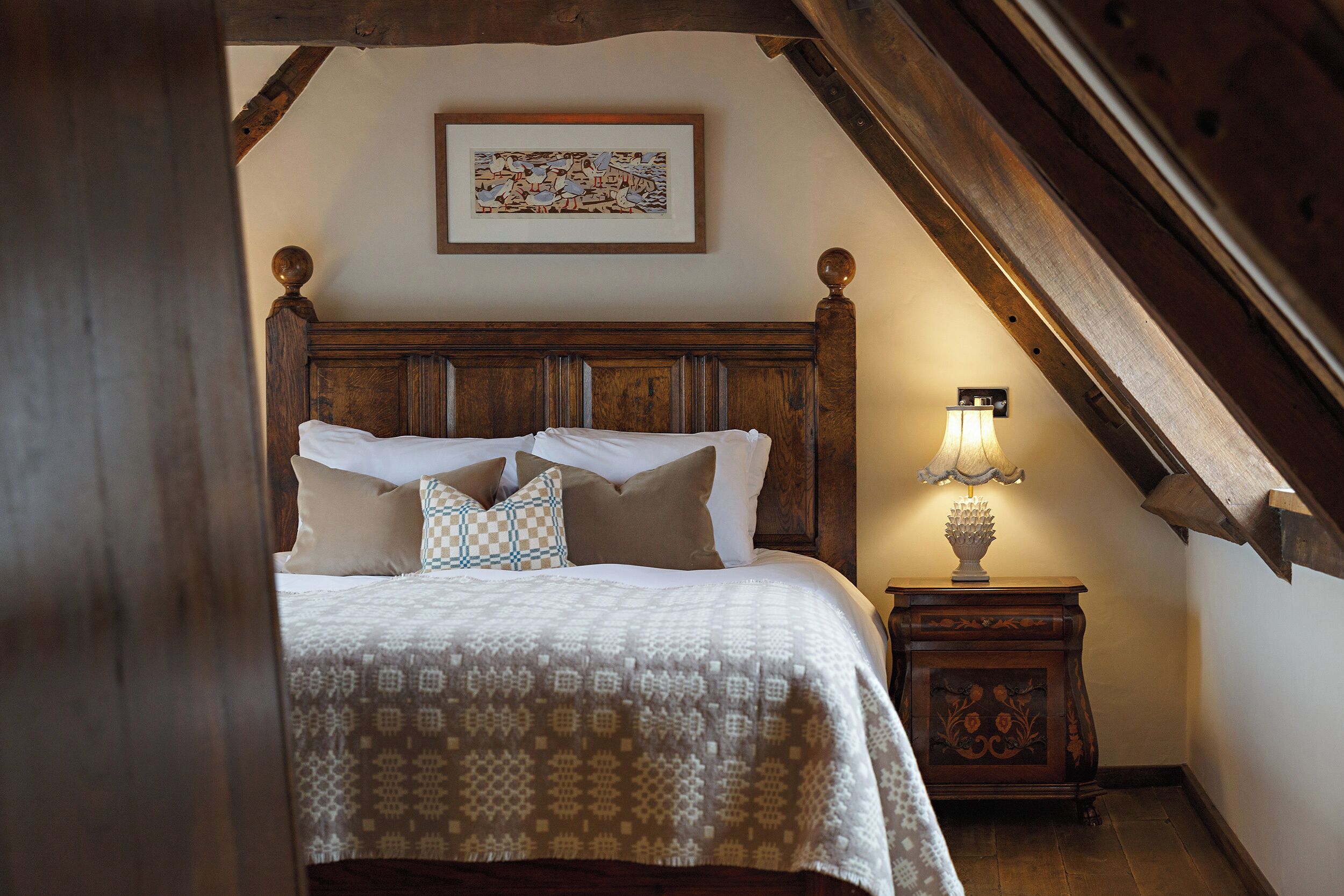 Un dormitorio con cabecera de madera, colcha estampada y mesita de noche con lámpara.