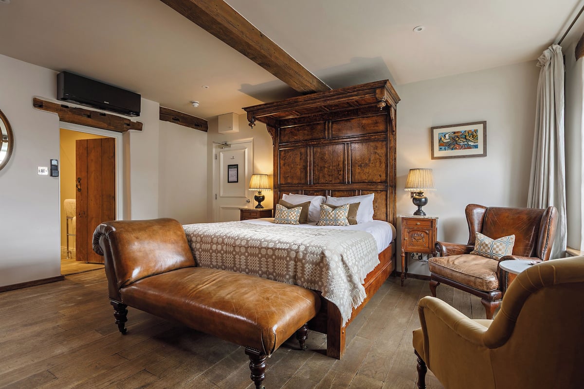 A spacious bedroom with a large wooden bed, a leather bench, and a classic armchair.