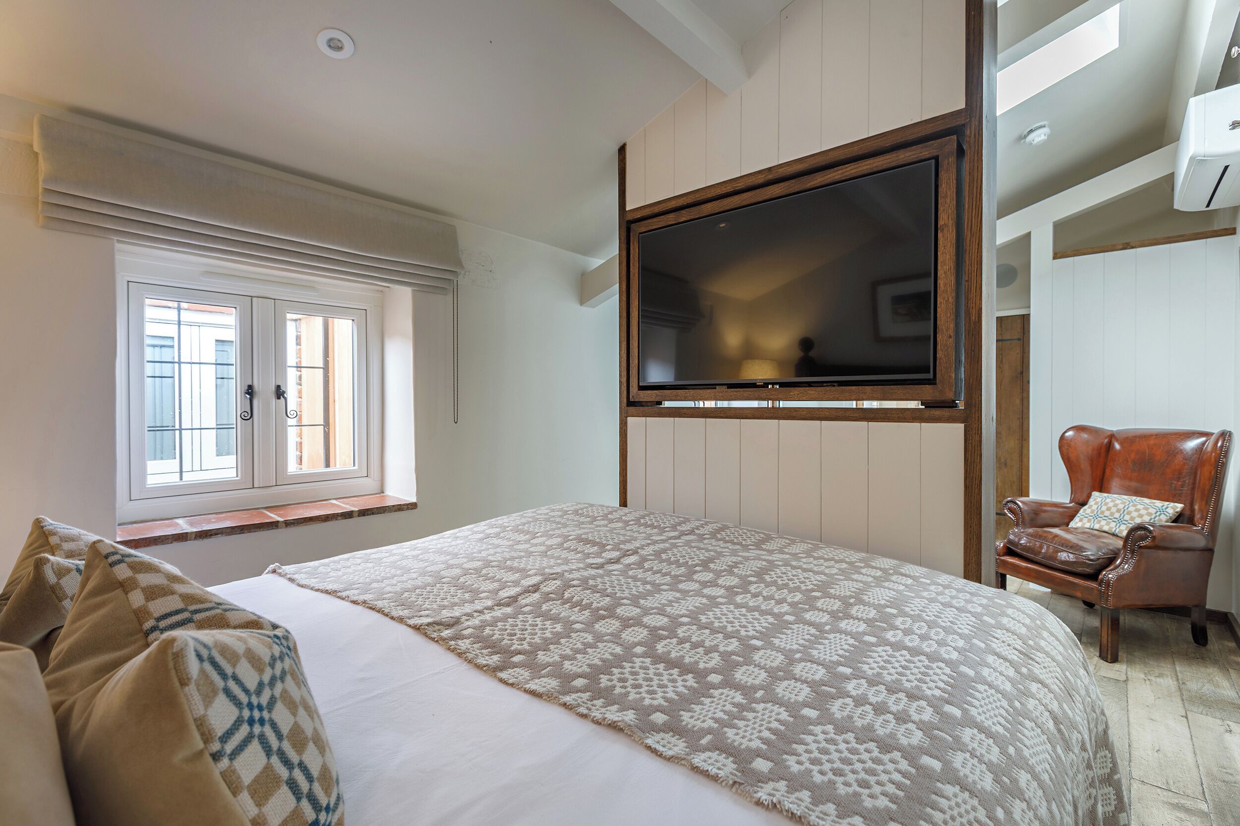 A bedroom with a large bed, a TV mounted on the wall, a window with curtains, and a chair.