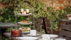 A wooden outdoor table set with a tiered dessert stand, plates, cups, and condiments. - Byfords  (Holt)