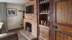 A living room with a brick fireplace, a television mounted above it, and a wooden door with a shelf above. - Byfords  (Holt)