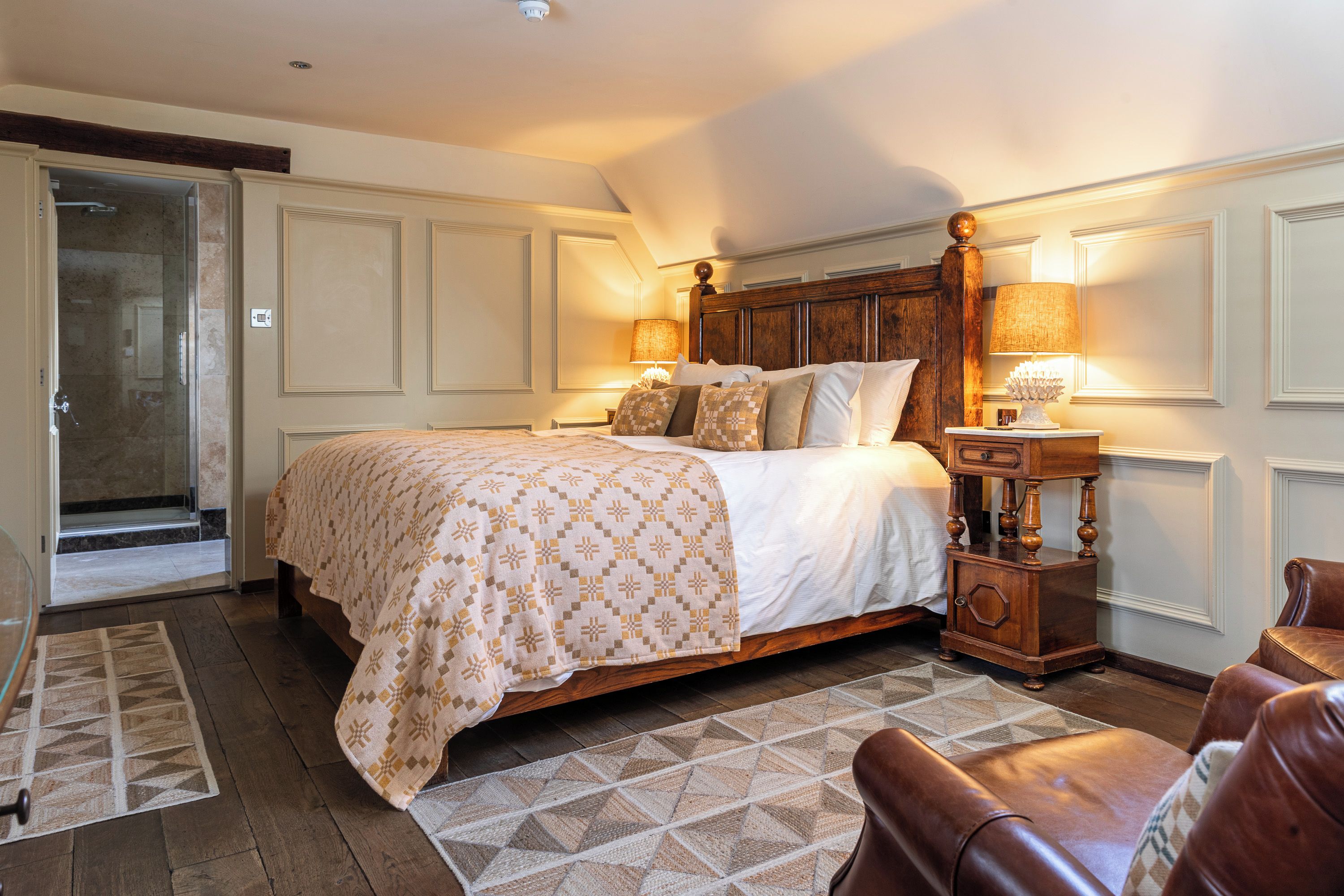 A bedroom with a large bed, a wooden nightstand, a chair, and a door leading to a bathroom.