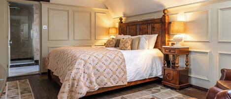 A bedroom with a large bed, a wooden nightstand, a chair, and a door leading to a bathroom.