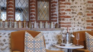 A cozy room with a brick wall, a window with metal bars, and a table with a bottle and glasses. - Byfords  (Holt)