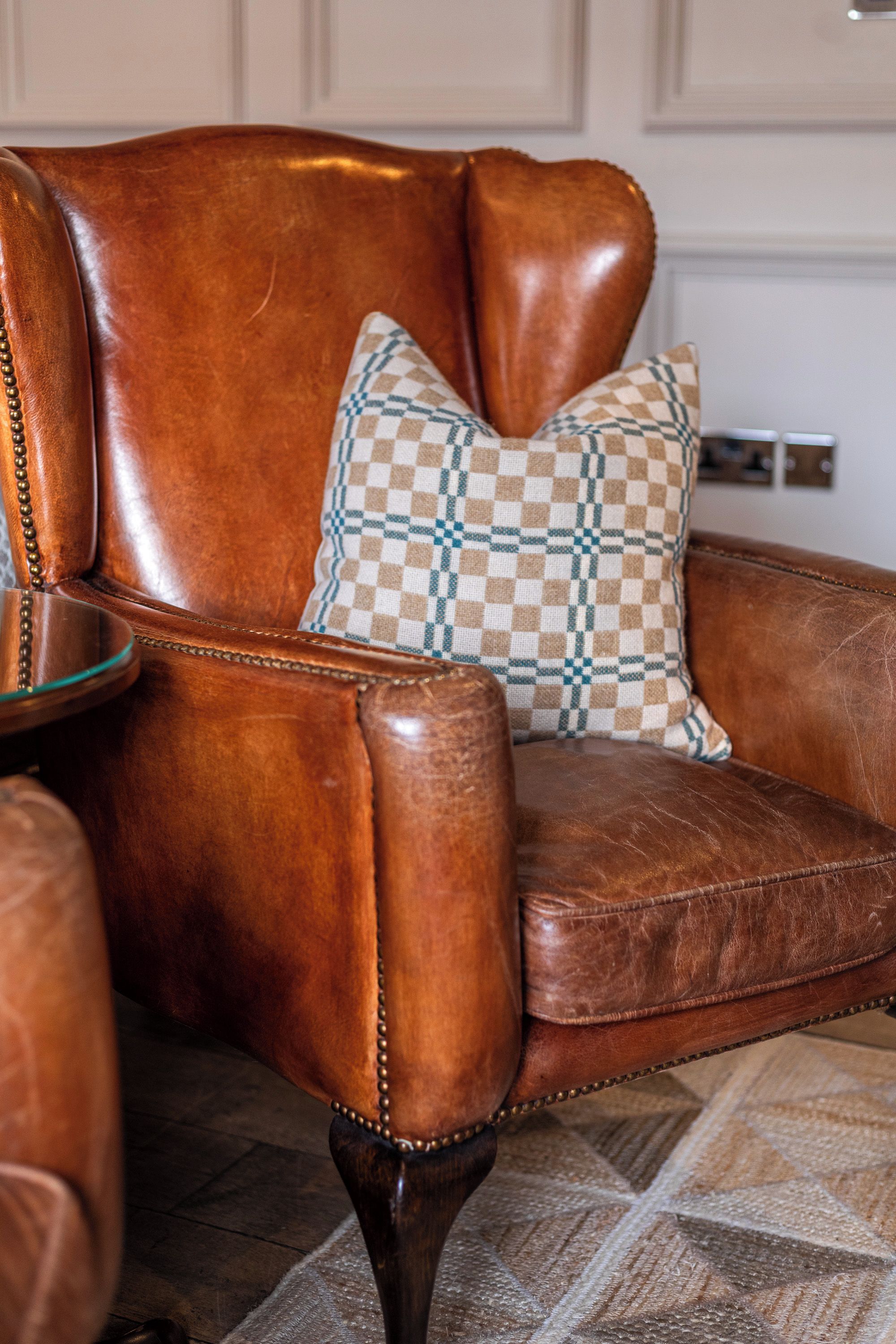 A brown leather armchair with a checkered pillow, a glass table, and a patterned rug.