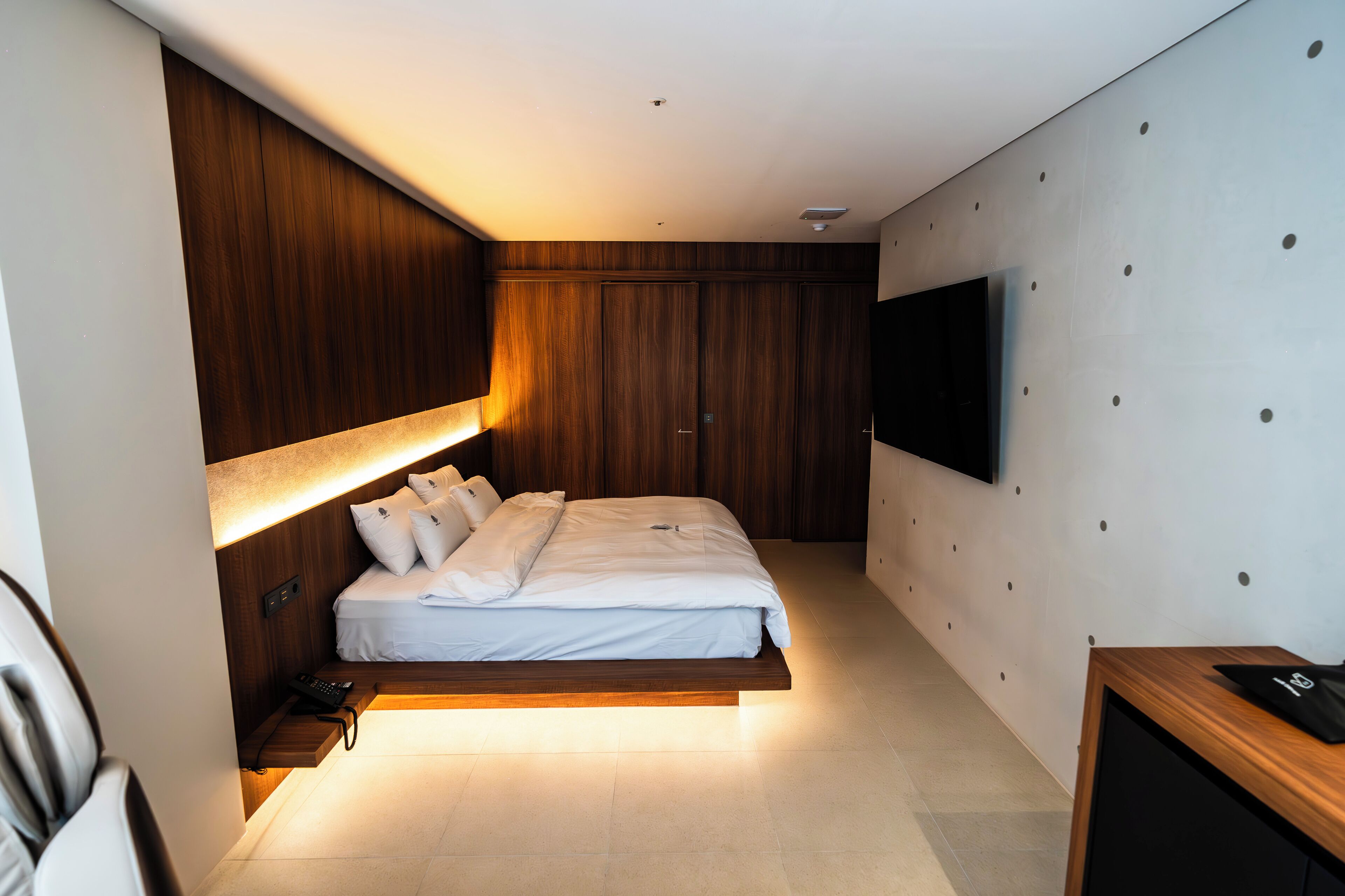 Un dormitorio moderno con cama, mesita de noche y televisor montado.