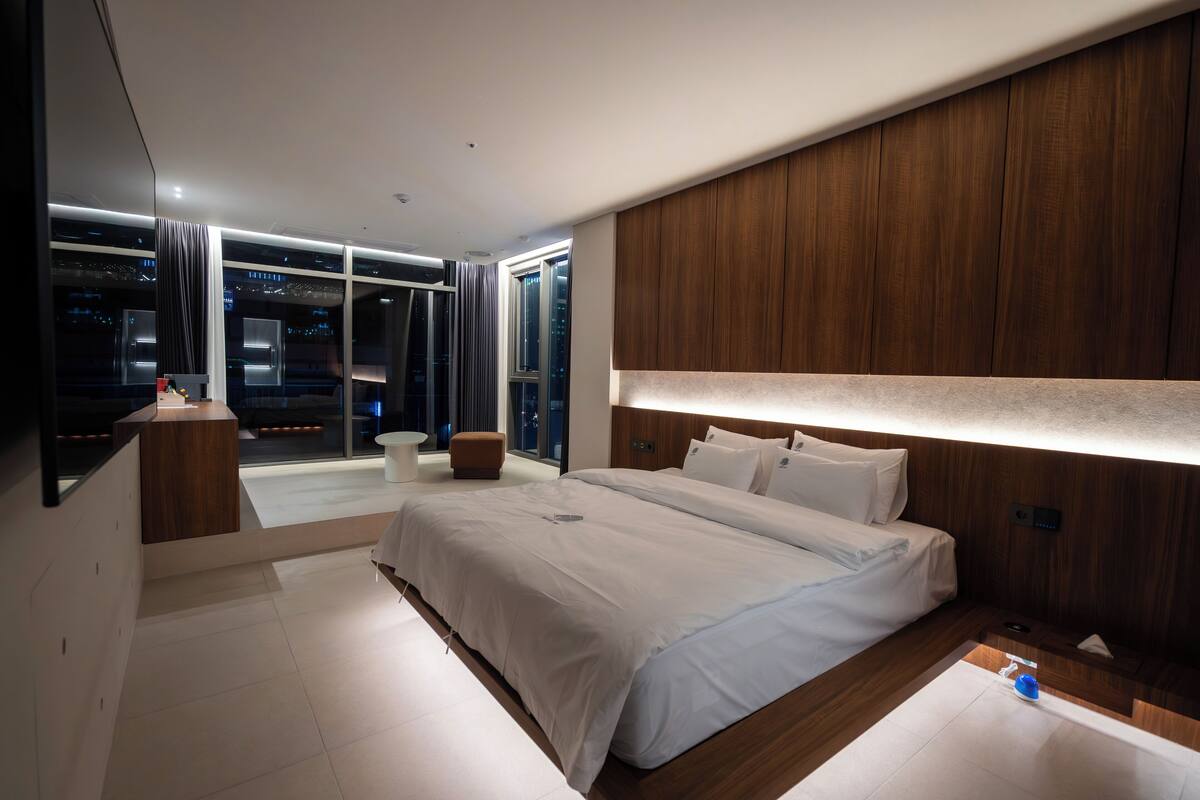 Habitación de hotel moderna con una cama grande, un escritorio y vistas a la ciudad de noche.