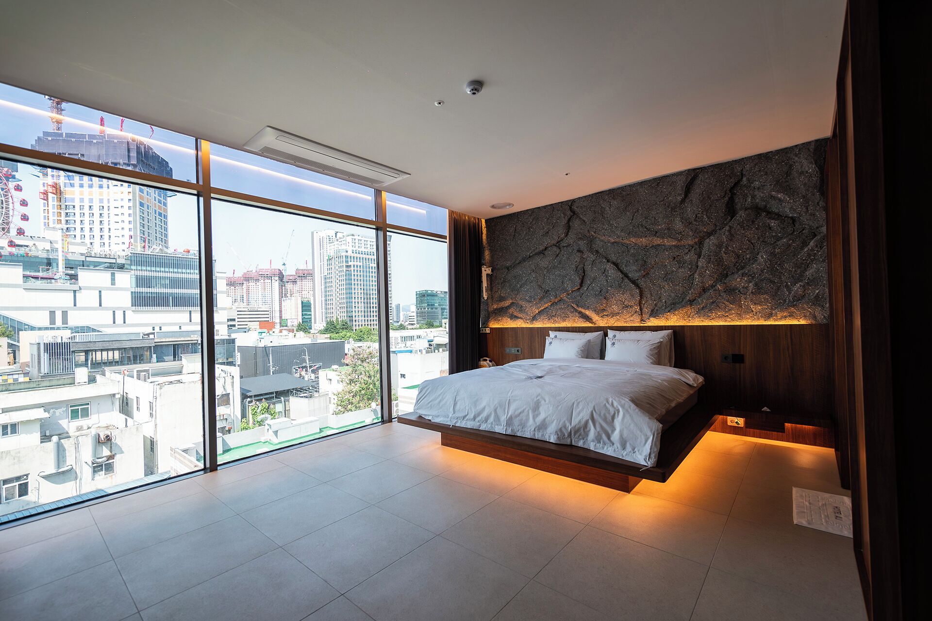 Quarto moderno com uma cama grande, vista da cidade através de janelas do chão ao teto e parede com textura.