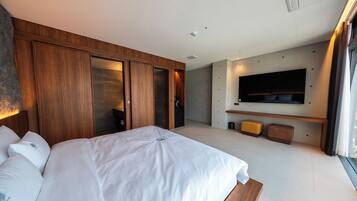 A modern hotel room with a large bed, wooden wardrobe, a flat-screen TV mounted on the wall, and a small seating area.