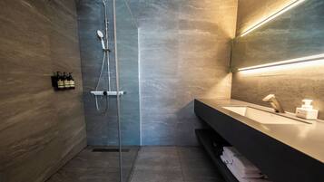 A modern bathroom with a glass-enclosed shower, a dark-toned vanity with a mirror, and a shelf with folded towels.