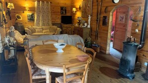 L’intérieur chaleureux d’un chalet avec une table à manger en bois, des chaises, un téléviseur et une cheminée.