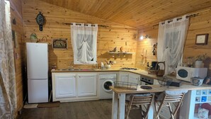 Une cuisine compacte aux murs en bois, équipée d’un réfrigérateur, d’un lave-linge et d’un petit coin repas avec des tabourets.