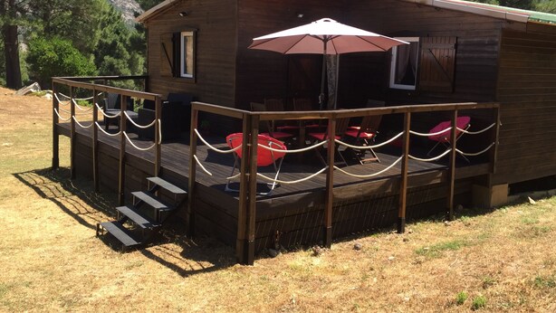 Une cabane en bois dotée d’une terrasse, de meubles de jardin et offrant une vue sur les montagnes.