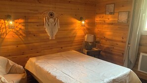 Une pièce de cabane en bois comprenant un lit, une chaise, une décoration murale et une petite table avec une lampe.