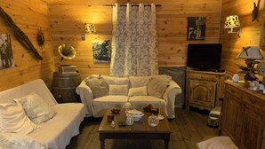 Un intérieur de chalet chaleureux avec deux canapés blancs, une table basse en bois, un téléviseur et un meuble contenant des objets décoratifs.