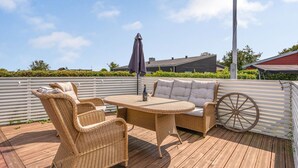 Une terrasse en bois, agrémentée de meubles en osier, notamment une table et des chaises, ainsi qu’une grande roue.
