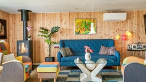 Un salon chaleureux avec un canapé bleu, des coussins colorés, une petite table, une plante en pot, une cheminée et un tapis aux couleurs vives.