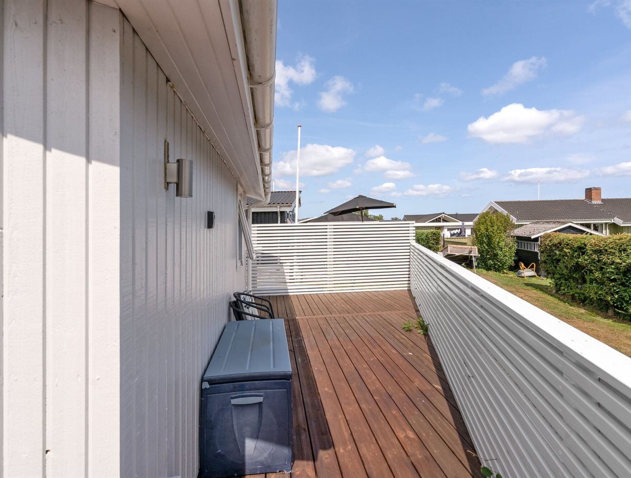 A wooden deck with a white railing, a black trash bin, and a clear sky.