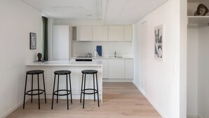 Une cuisine moderne avec des meubles blancs, un îlot central doté de tabourets et un petit coin bar.