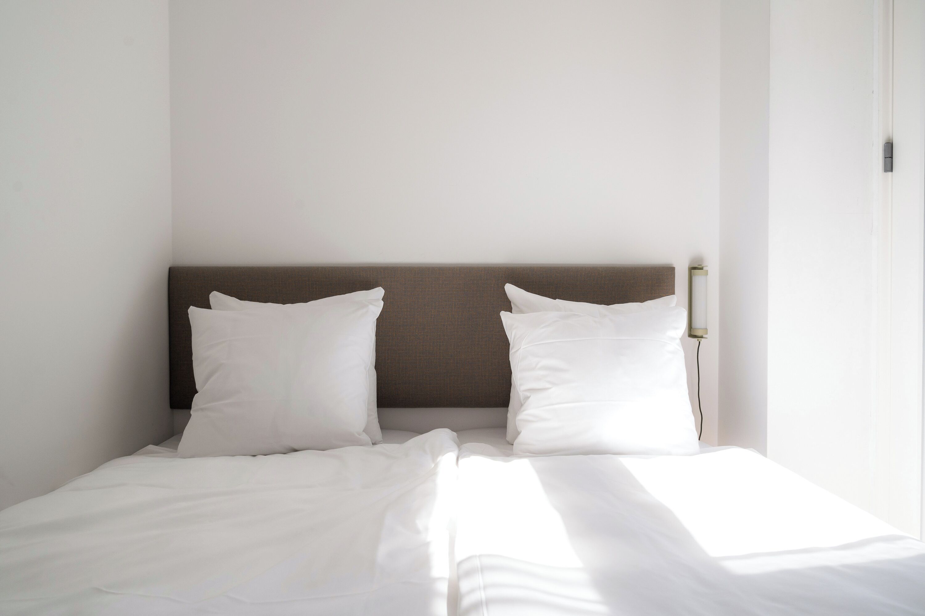 A neatly made bed with white linens and a brown headboard in a hotel room.