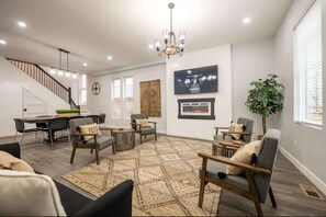 A spacious living area with a staircase, a dining table, multiple chairs, a large rug, and a television mounted on the wall.