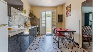 A compact kitchen with a tiled backsplash, a dining area with a table and chairs, and a view through an open door.
