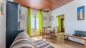 A cozy living room with a sofa, dining table, and chairs, wooden floors, and a TV on a wooden stand.