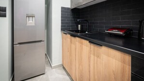 Une cuisine moderne dotée d’un réfrigérateur en acier inoxydable, de meubles en bois, d’un plan de travail noir et d’un pare-feu noir.