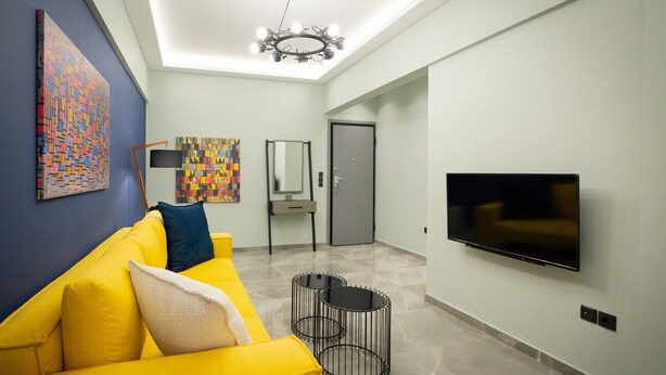 Un salon moderne avec un canapé jaune, un téléviseur à écran plat et des œuvres d’art abstraites accrochées aux murs.
