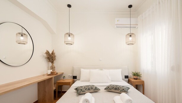 Ein Hotelzimmer mit einem Bett, zwei Nachttischen, einem runden Spiegel, einer Wandklimaanlage und zwei Pendelleuchten.