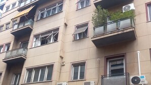 Ein mehrstöckiges Gebäude mit Balkonen, Klimaanlagen und einem Schaufenster, vor dem ein Motorrad geparkt ist.
