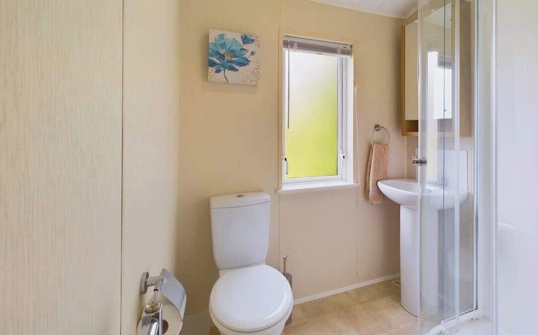 Une salle de bain comprenant des toilettes, un lavabo, une douche en verre et une fenêtre.