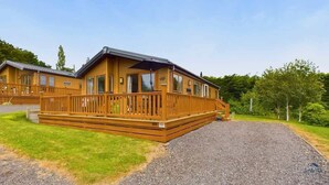 Une cabane en bois dotée d’une terrasse, de grandes fenêtres et d’une allée gravillonnée.