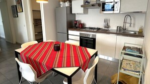 A modern kitchen with white cabinets, a microwave, a stove, and a sink. There is a dining table with a red tablecloth and white chairs.